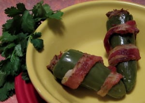 Bacon wrapped stuffed jalapeños in a yellow bowl.