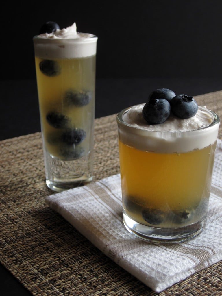 Two miniature dessert glasses filled with yellow gelatin, blueberries, and topped with cream.