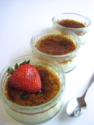 Three glass dishes of crème brûlée with a strawberry half on the nearest dish.