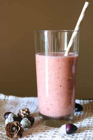 A pink drink with red flecks throughout in a glass jar with a striped paper straw inserted.