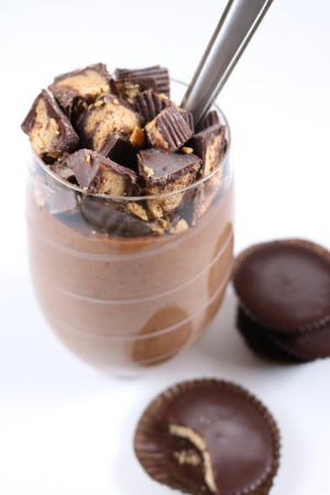Chocolate pudding in a stemless wine glass topped with roughly chopped peanut butter cups with more peanut butter cups stacked to the side out of focus.
