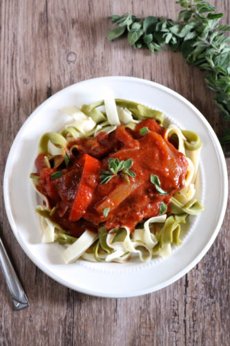 A plate of noodles. Steak on top is fully covered with red sauce and a little fresh oregano. More oregano to the side of the plate.