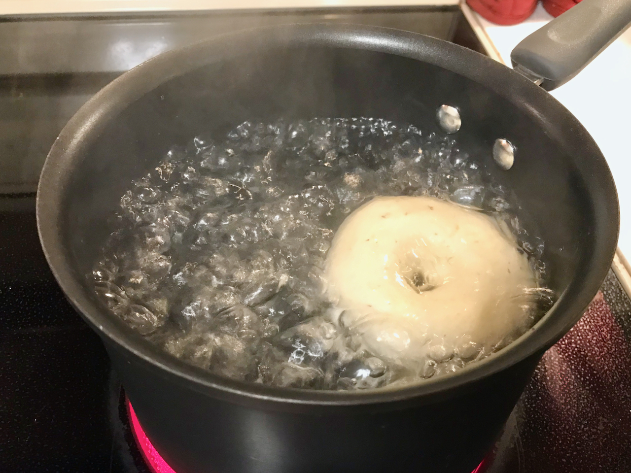 A single bagel boiling in a pot of water.