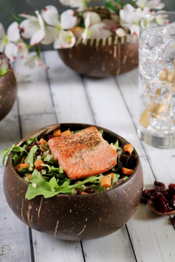 Salmon salad with a glass of water and bowl of flowers behind it.