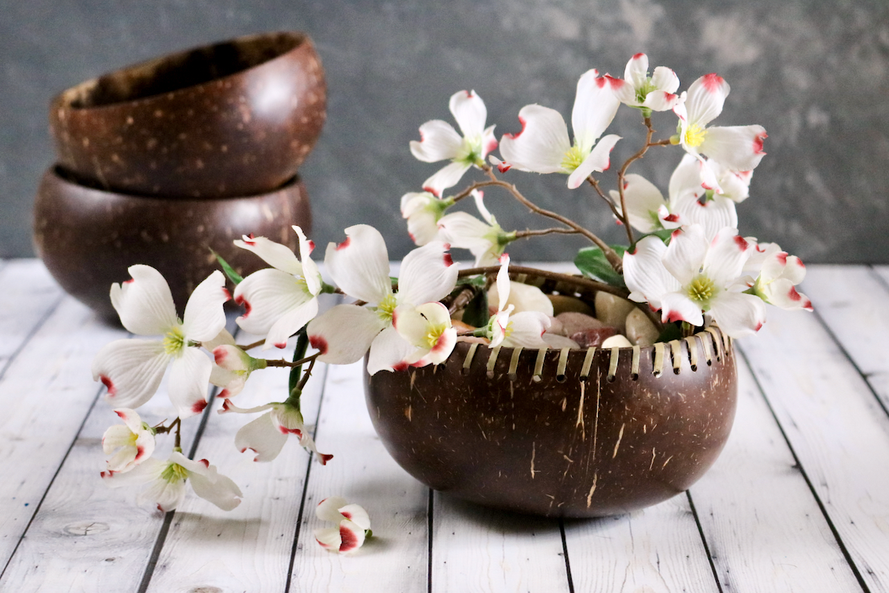 A coconut shell bowl being used to display decorative rocks and artificial flowers.
