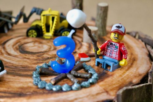 A Lego minifigure holding a stick with a marshmallow over an unlit candle shaped like a 3.
