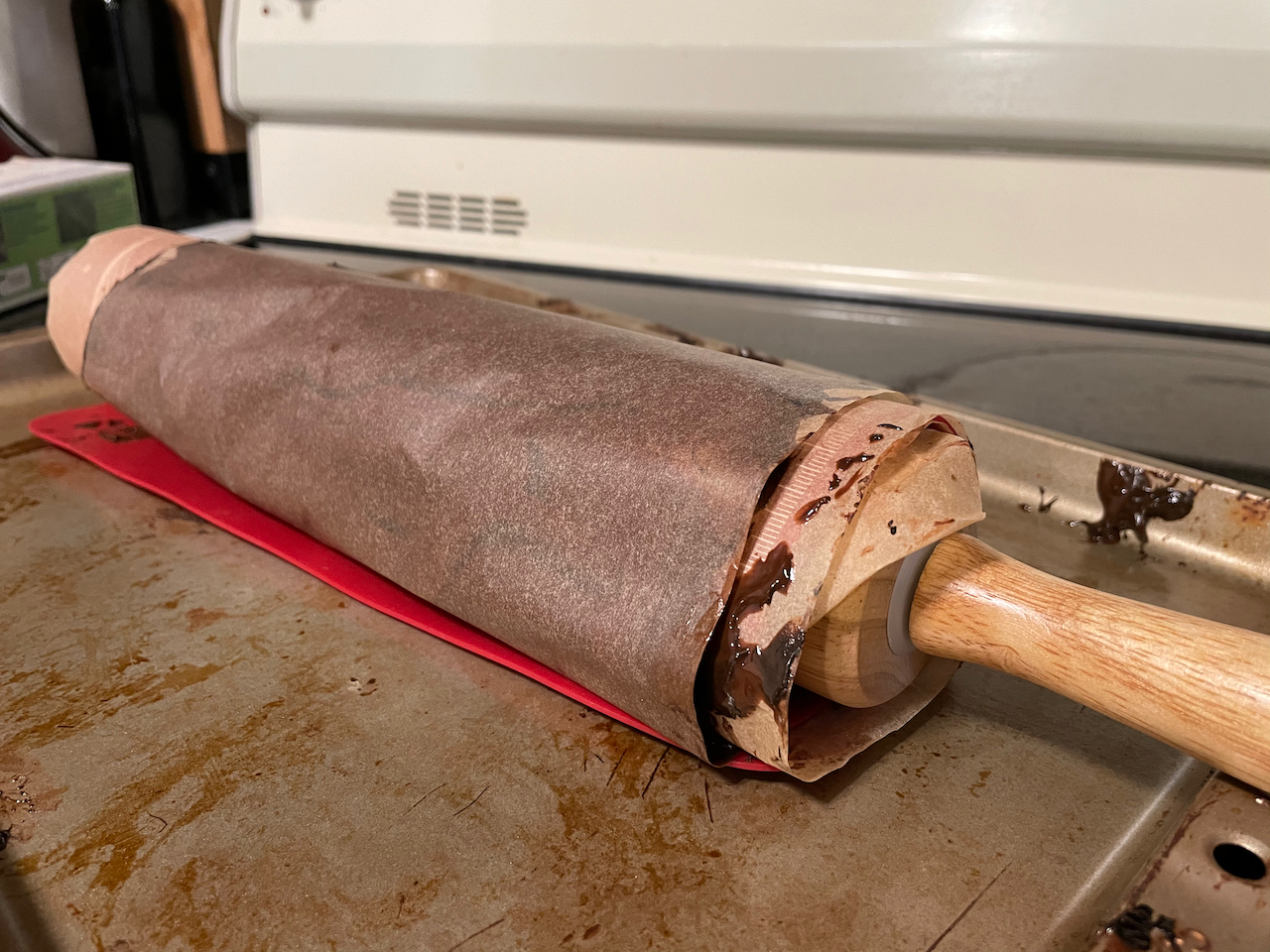 Parchment paper with melted chocolate wrapped around a wooden rolling pin on top of a cookie sheet.