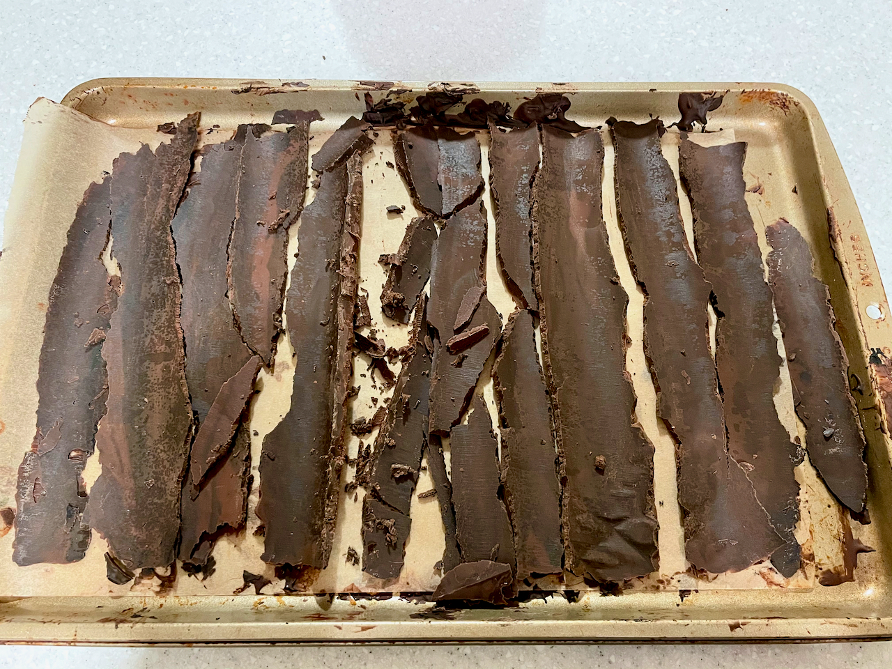 Still smooth chocolate bark shards laying vertically atop a parchment lined baking sheet.