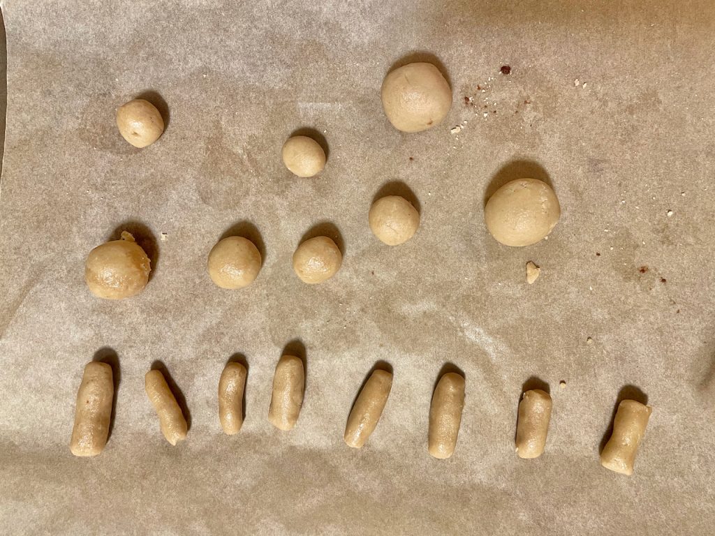 Unbaked cookie dough in the shape of small balls and stems on parchment paper.