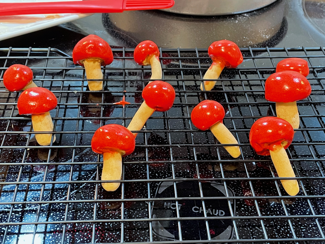 Small cookies in the shape of mushrooms with red caps are set on a cooling rack.