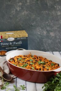 An oval, burgundy colored casserole dish containing taco noodle casserole sprinkled with cilantro. Pasta package is in the background.