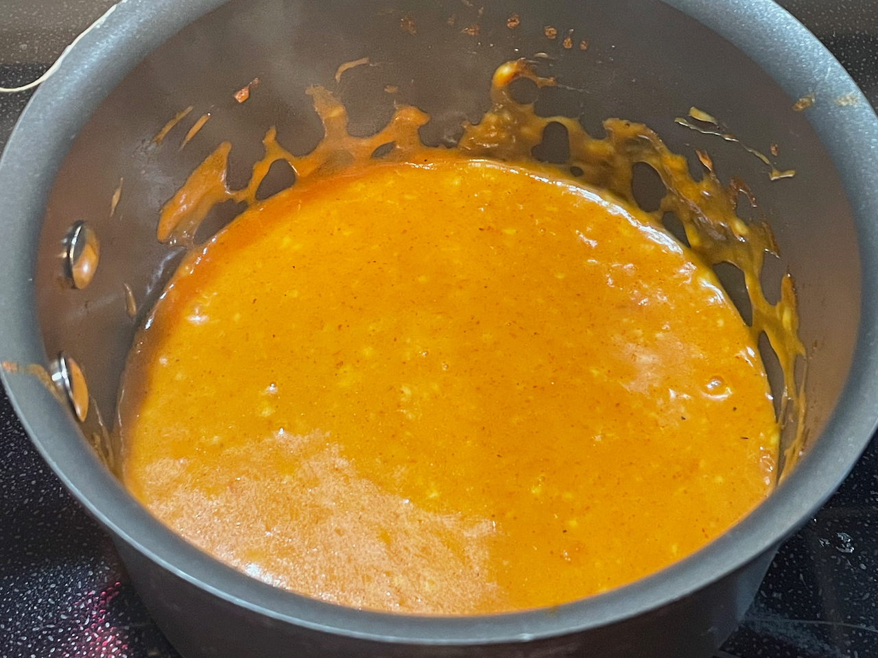 Orange colored sauce in a black pot.