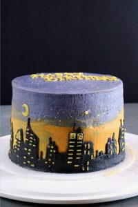 A round cake with a buttercream sunset, moon, planet, and city skyline on the side.