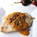 A fillet of tilapia coated in a thick orange sauce and topped with seeds.
