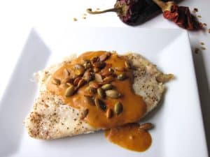 A fillet of tilapia coated in a thick orange sauce and topped with seeds.